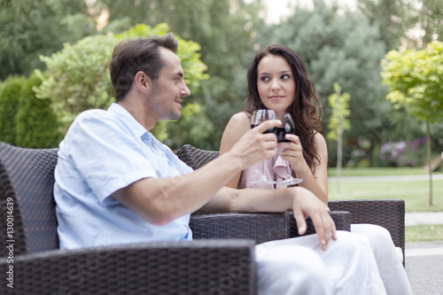 Loving young couple toasting red wine on chairs in park