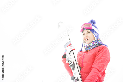 Smiling young woman carrying skis in snow
