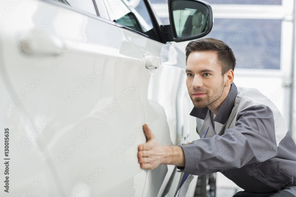 Young maintenance engineer examining car in repair shop Young maintenance engineer examining car in repair shop