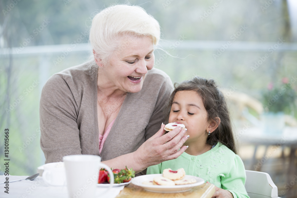 Happy senior woman feeding cookie to granddaughter at home