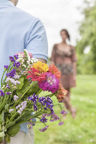 Cropped image of man hiding bouquet from woman in park