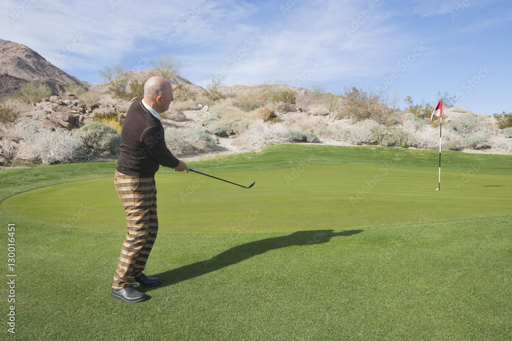 Full length side view of senior male golfer swinging his club at golf course Full length side view of senior male golfer swinging his club at golf course