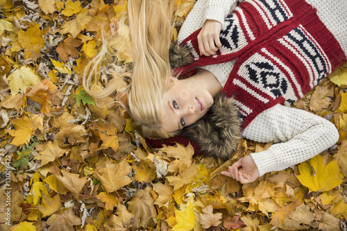 High angle portrait of young woman lying on autumn leaves in park