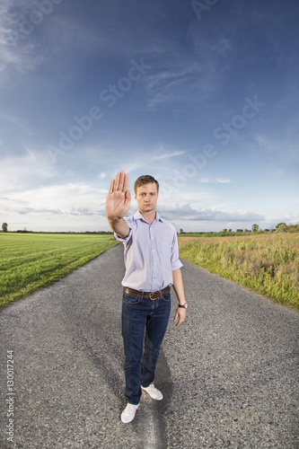 Full length portrait of young man making stop gesture at country road