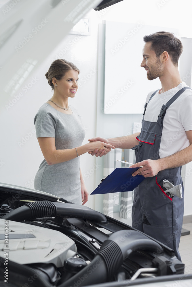 Young repair worker shaking hands with customer in car workshop Young repair worker shaking hands with customer in car workshop