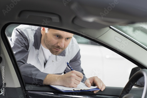 Male mechanic with clipboard checking car's interior in repair shop
