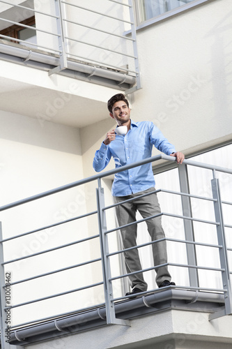 Full length of young businessman having coffee at hotel balcony