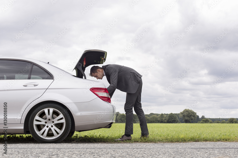 Φωτογραφία Full length side view of young businessman looking in car trunk at countryside