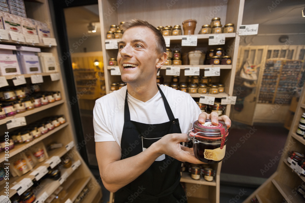 Cheerful salesman holding jar of jam in grocery store