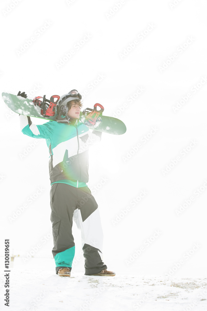 Naklejka premium Full length of young man carrying snowboard in snow