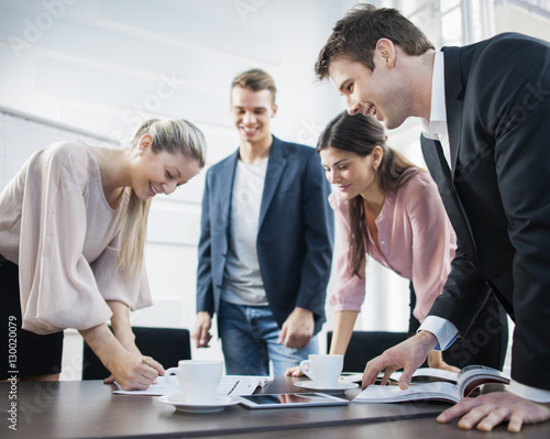 Canvas Print Happy young business people brainstorming at conference table