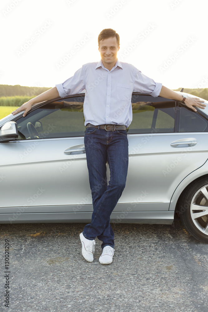 Full length portrait of smiling young man leaning on car at countryside Full length portrait of smiling young man leaning on car at countryside