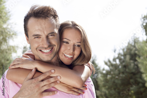 Portrait of happy young man being embrace by woman from behind in park