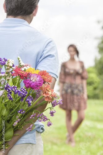 Cropped image of man surprising woman with bouquet in park