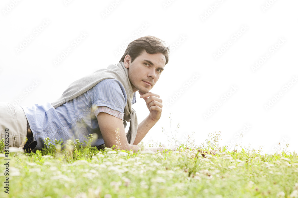 Portrait of young man lying on grass against clear sky Portrait of young man lying on grass against clear sky