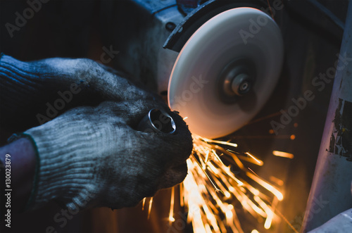 Factory worker at workshop grinding steel rod with abrasive disc and flying sparks