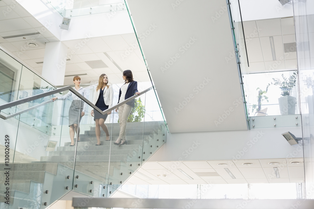 Businesswomen conversing while moving down steps in office Businesswomen conversing while moving down steps in office