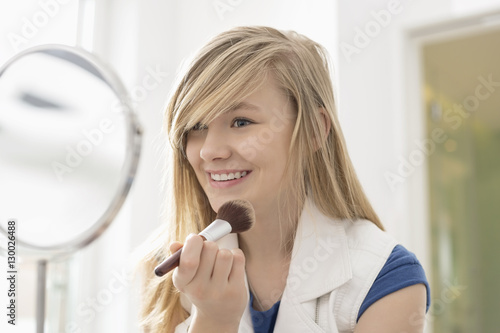 Girl applying makeup in front of mirror at home