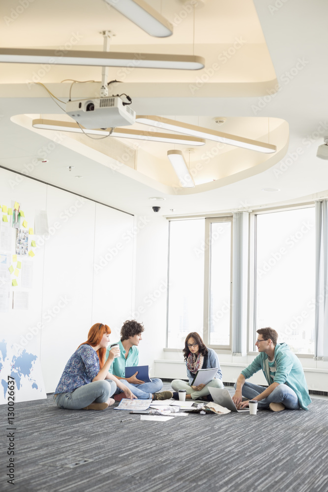 Businesspeople discussing while sitting on floor in creative office Businesspeople discussing while sitting on floor in creative office