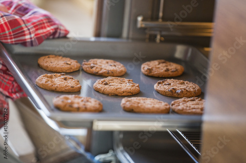 Cropped image of hand removing cookie tray from oven in kitchen photo