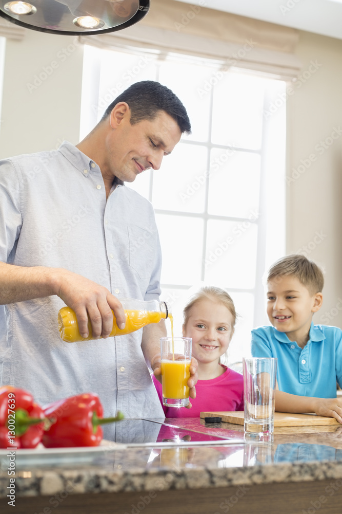 Father serving orange juice for children in kitchen