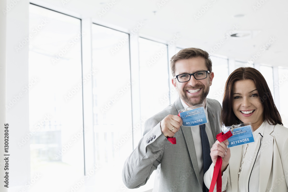 Portrait of happy business people showing identity cards in convention center