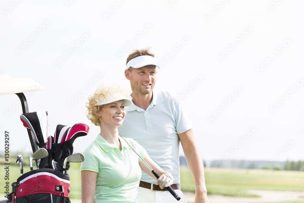 Naklejka premium Smiling golfers standing at golf course against clear sky