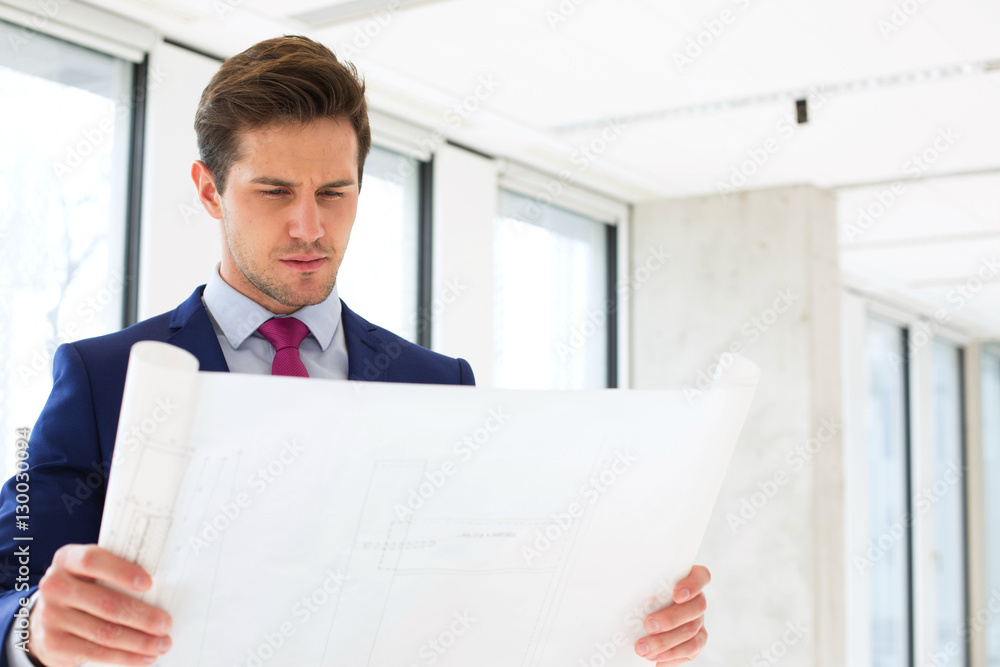 Confident young businessman reading blueprint in new office Confident young businessman reading blueprint in new office
