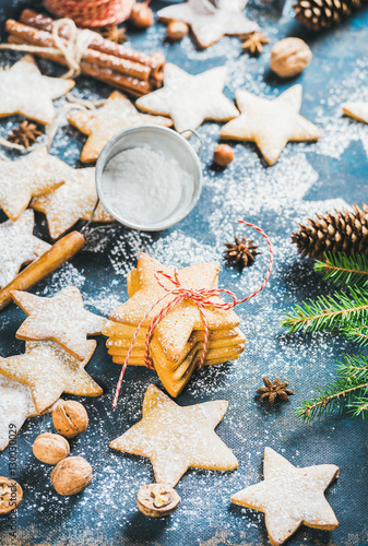 Gingerbread star shaped cookies with cinnamon, anise and nuts served with fir-tree branch and pine cones on dark plywood background, selective focus, vertical composition