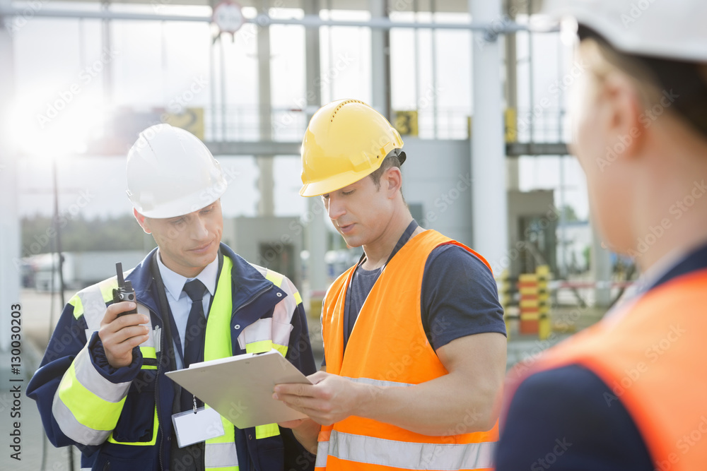 Workers discussing over clipboard in shipping yard Workers discussing over clipboard in shipping yard