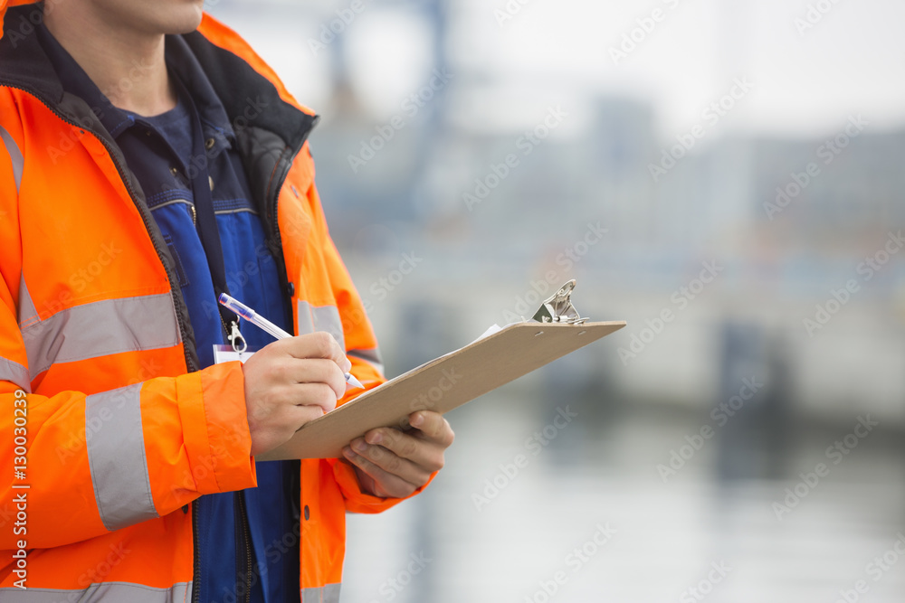 Midsection of mid adult man writing on clipboard in shipping yard Midsection of mid adult man writing on clipboard in shipping yard