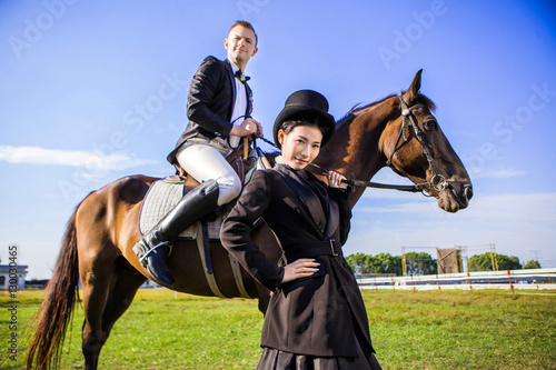 Portrait of confident woman standing by man sitting on horse at field