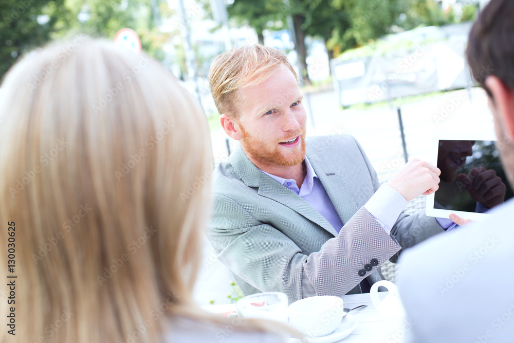 Businessman discussing over digital tablet with colleagues at sidewalk cafe Businessman discussing over digital tablet with colleagues at sidewalk cafe