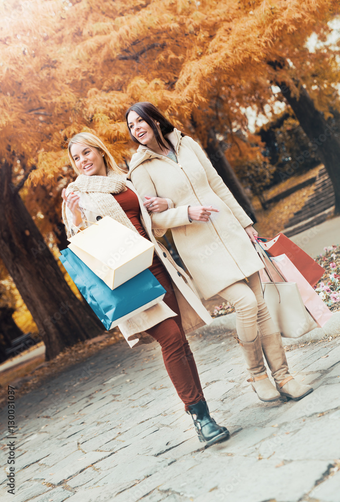 Two beautiful girls in autumn park after shopping. Consumerism a