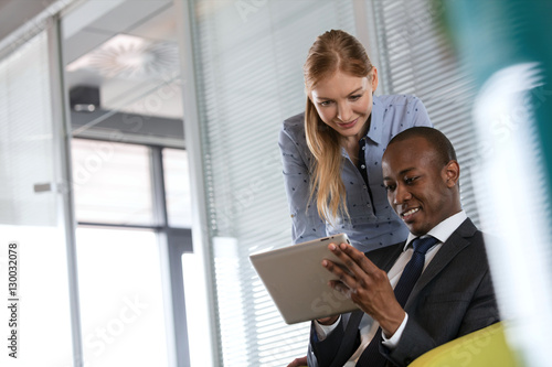 Smiling young businesswoman with male colleague using digital tablet in office
