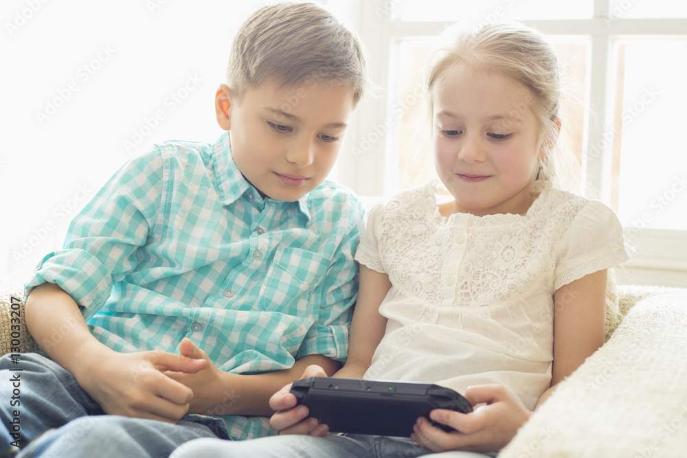Siblings playing hand-held video game at home Siblings playing hand-held video game at home