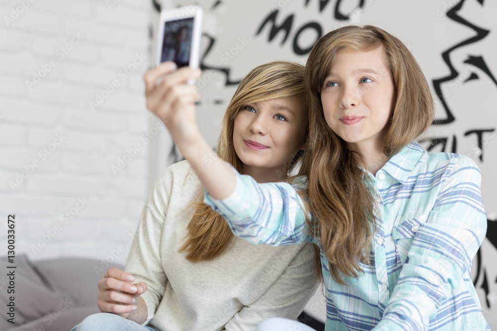 Cute sisters taking photos with smart phone at home Cute sisters taking photos with smart phone at home