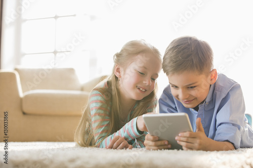 Brother and sister using digital tablet on floor at home © moodboard