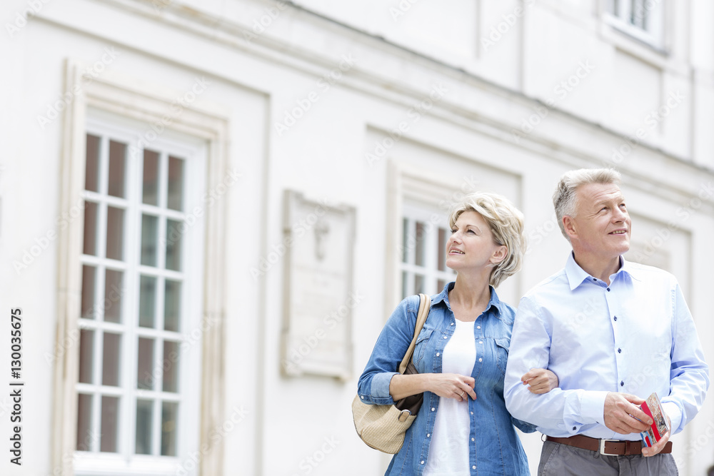 Smiling middle-aged couple standing with arm in arm outside building Smiling middle-aged couple standing with arm in arm outside building