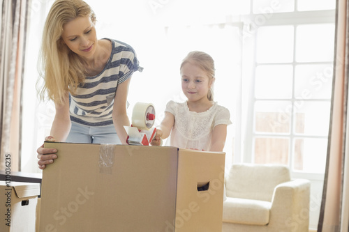 Mother and daughter packing cardboard box at home