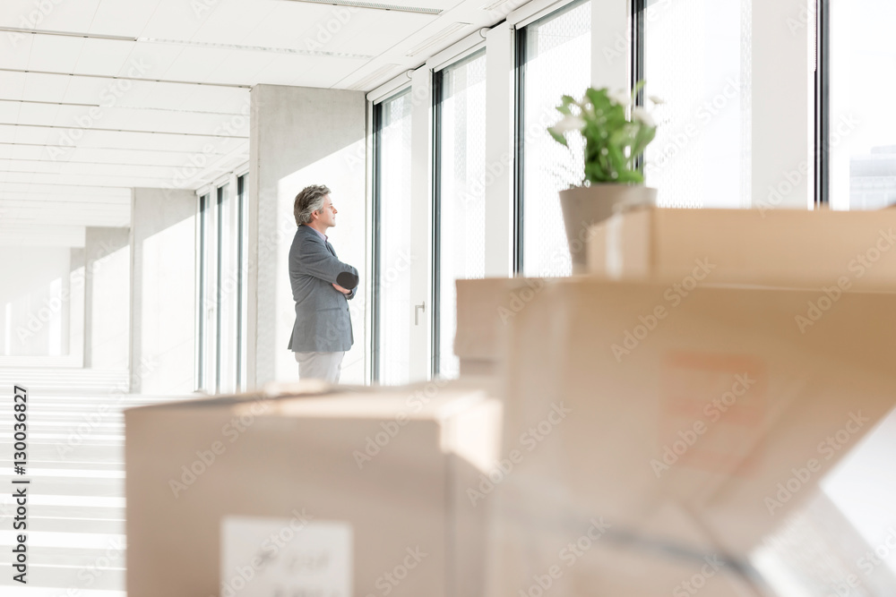 Distant image of businessman looking through window with cardboard boxes in foreground