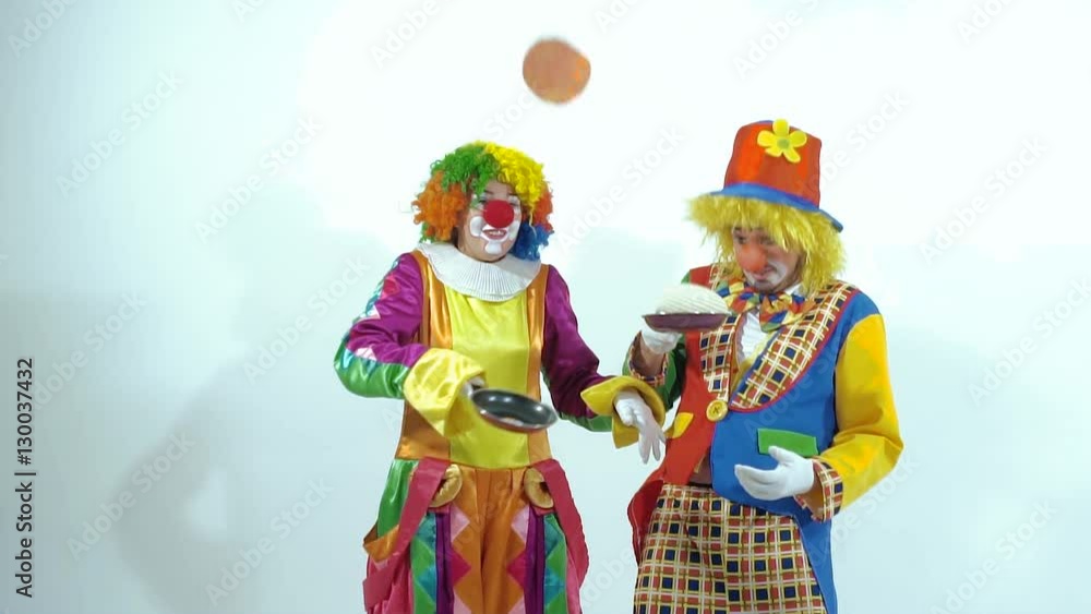 A couple of funny clowns holding small frying pans play with pancakes A couple of funny clowns holding small frying pans play with pancakes
