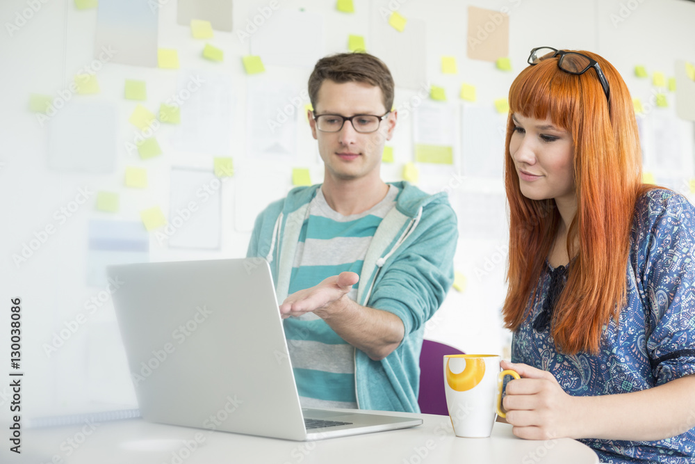 Businessman showing something to female colleague on laptop in creative office Businessman showing something to female colleague on laptop in creative office