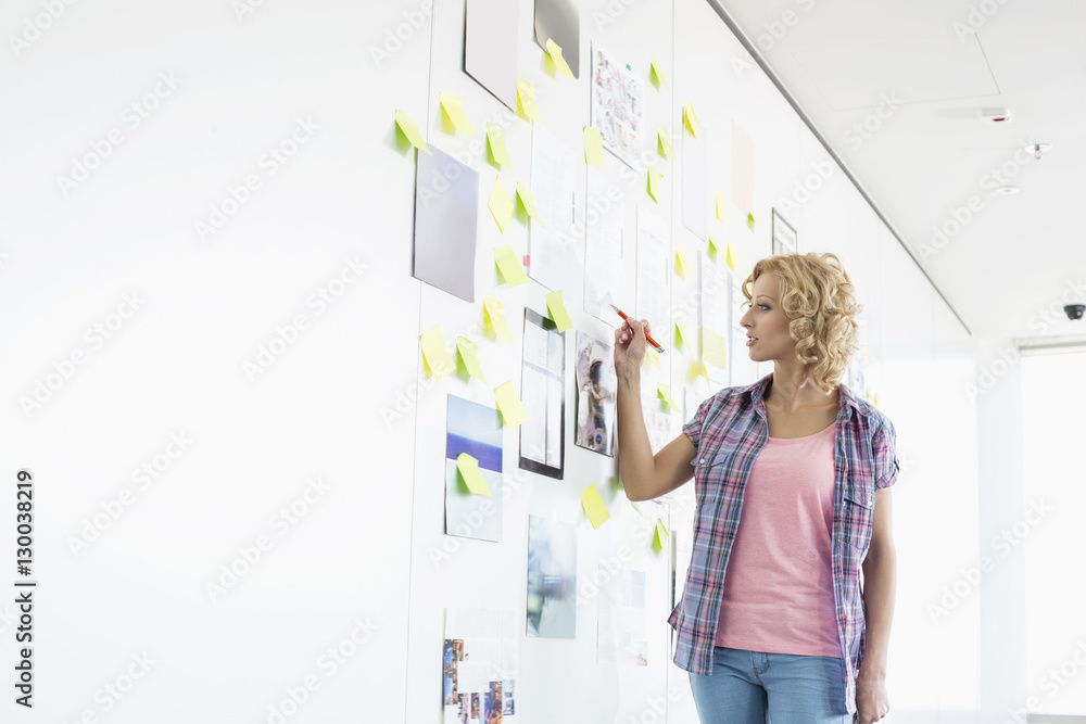 Creative businesswoman writing on sticky paper in office Creative businesswoman writing on sticky paper in office