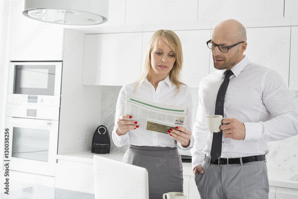 Mid adult business couple reading newspaper while having coffee in kitchen Mid adult business couple reading newspaper while having coffee in kitchen
