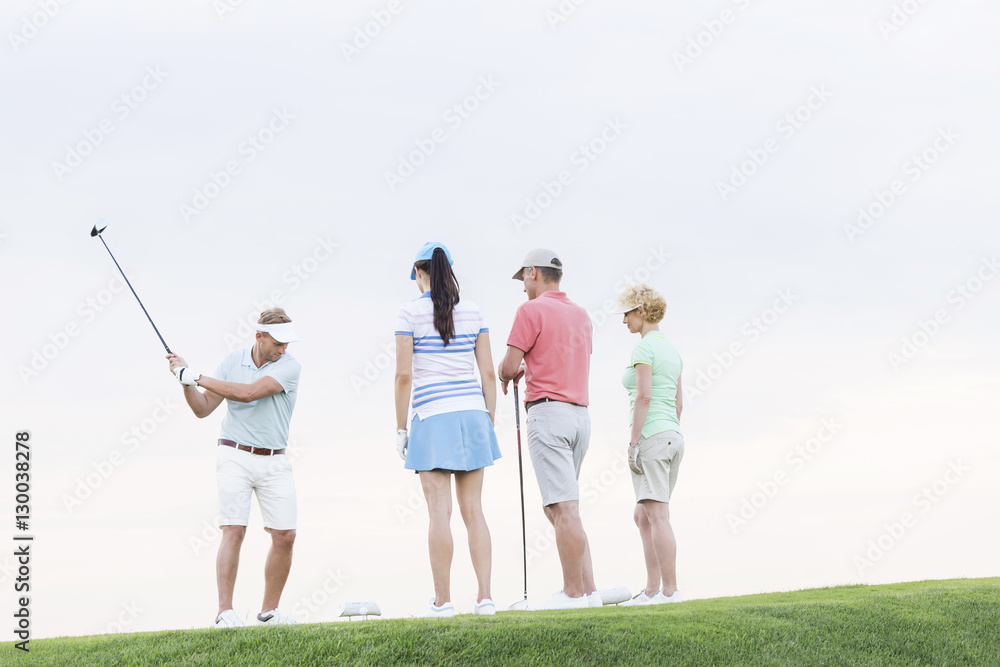 Obraz premium Group of friends looking at man playing golf against clear sky
