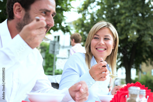 Happy businesswoman eating food with colleague at sidewalk cafe