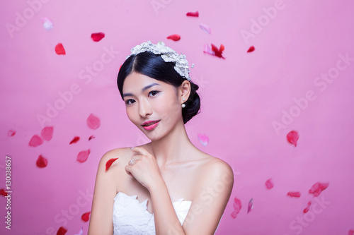 Portrait of beautiful bride with rose petals in mid-air against pink background