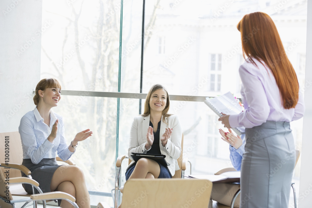 Happy businesswomen clapping for colleague after presentation in office Happy businesswomen clapping for colleague after presentation in office