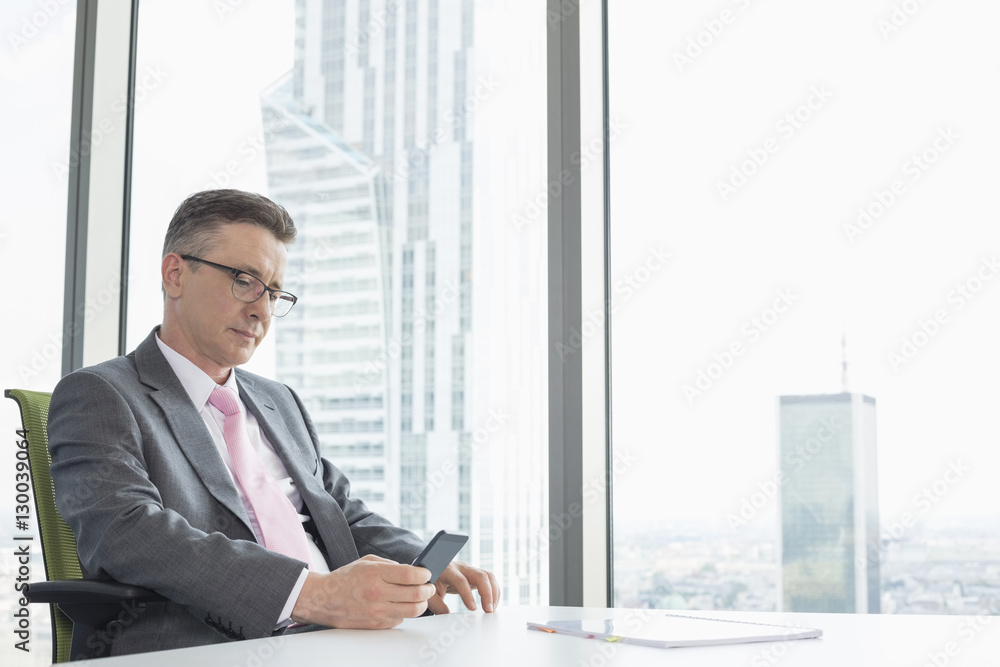 Mature businessman text messaging through cell phone near office window Mature businessman text messaging through cell phone near office window
